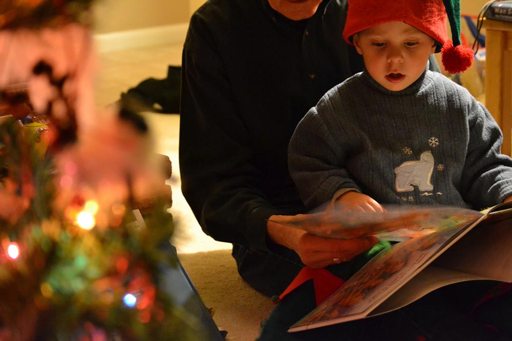 Kid sitting on grandparent's lap reading at Christmas